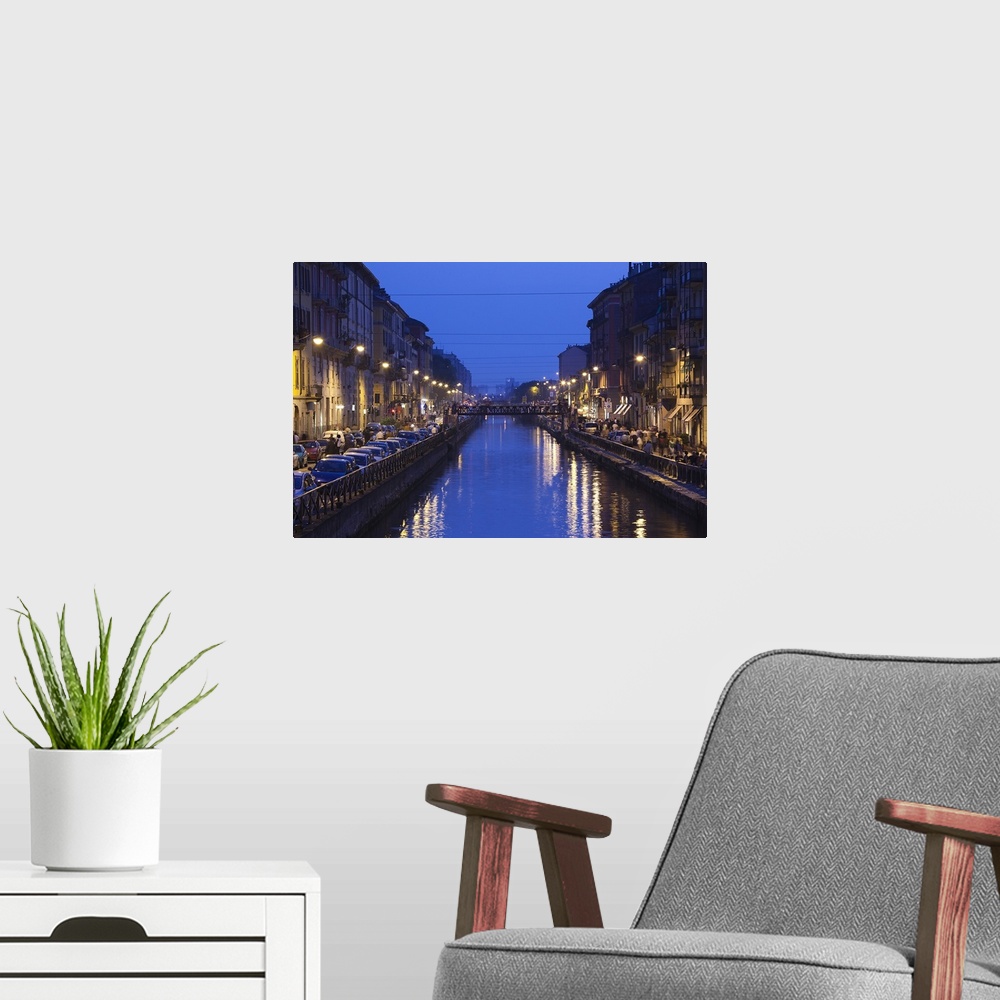 A modern room featuring Landscape photograph on giant wall hanging, looking down a canal that is lit from both sides, as ...