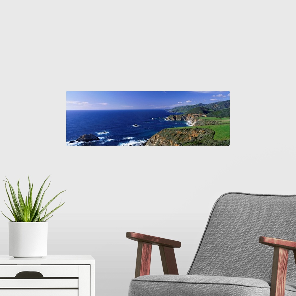 A modern room featuring This wall art is a panoramic photograph of the coastal cliffs and the open ocean beyond.