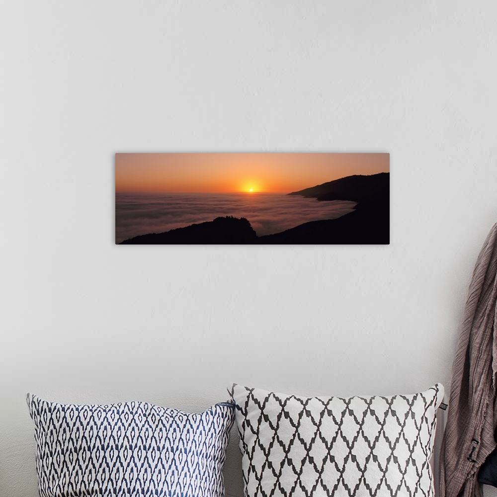 A bohemian room featuring A large panoramic piece of a sunset with a fog mist over the water and mountains lining the right...