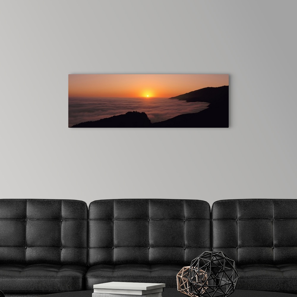 A modern room featuring A large panoramic piece of a sunset with a fog mist over the water and mountains lining the right...