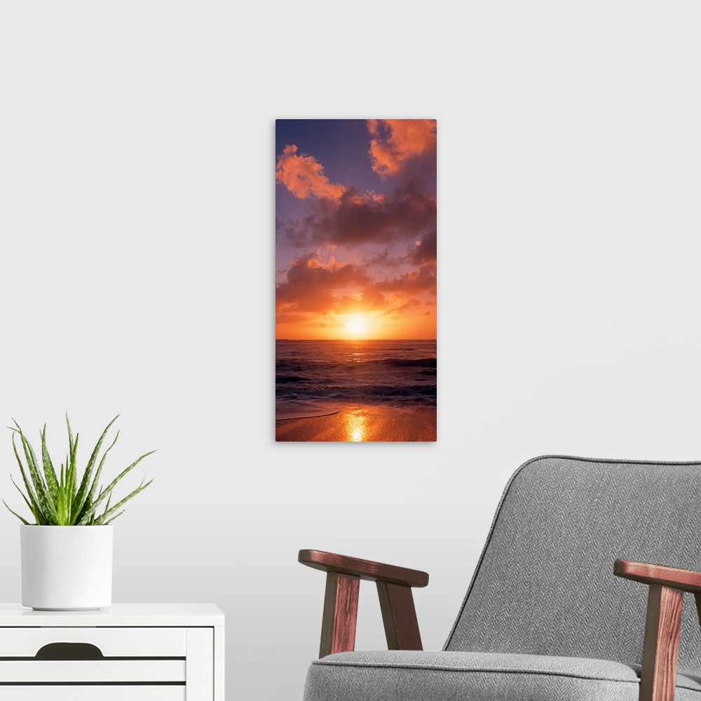 A modern room featuring This vertical photograph shows the sun setting at the beach as waves wash against the shore.