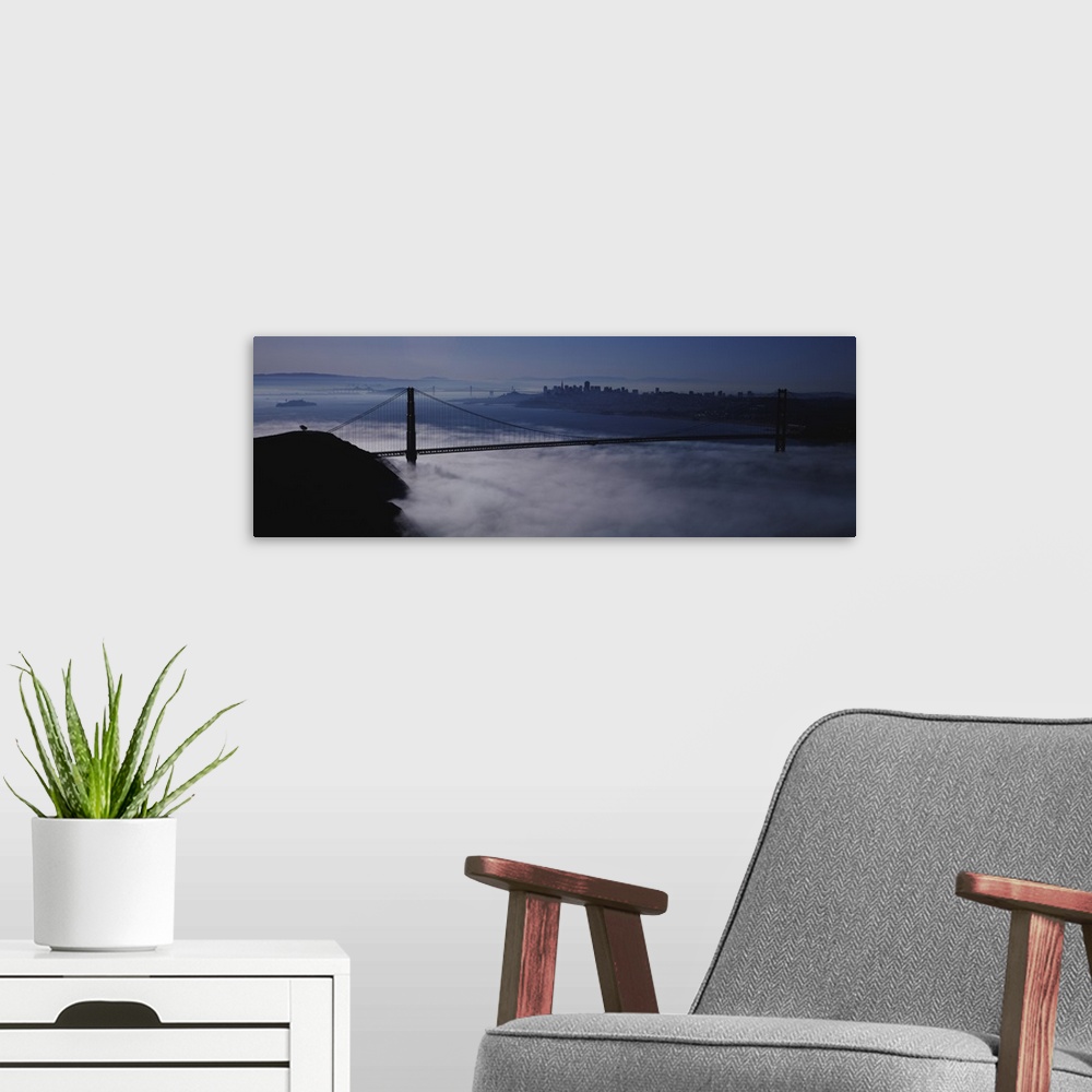A modern room featuring Large panoramic piece of the Golden Gate bridge that has dense fog just under it covering the wat...