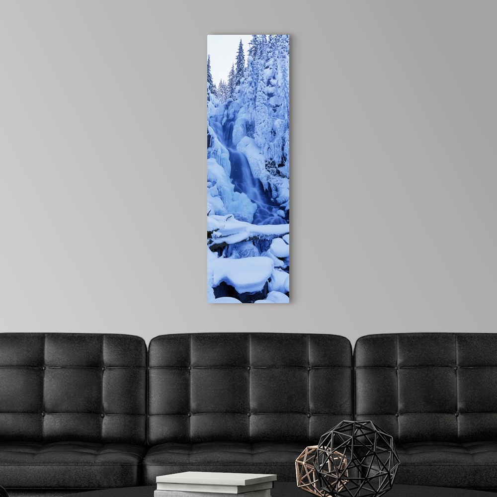 A modern room featuring A tall panoramic piece of a frozen waterfall that is surrounded by trees and rocks that are cover...