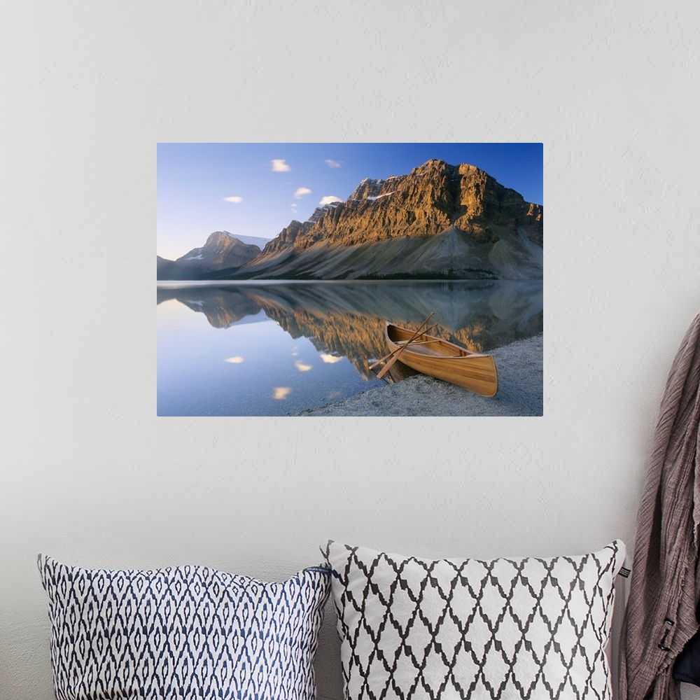A bohemian room featuring Oversized photography artwork of a canoe sitting on the edge of water with mountains in the backg...