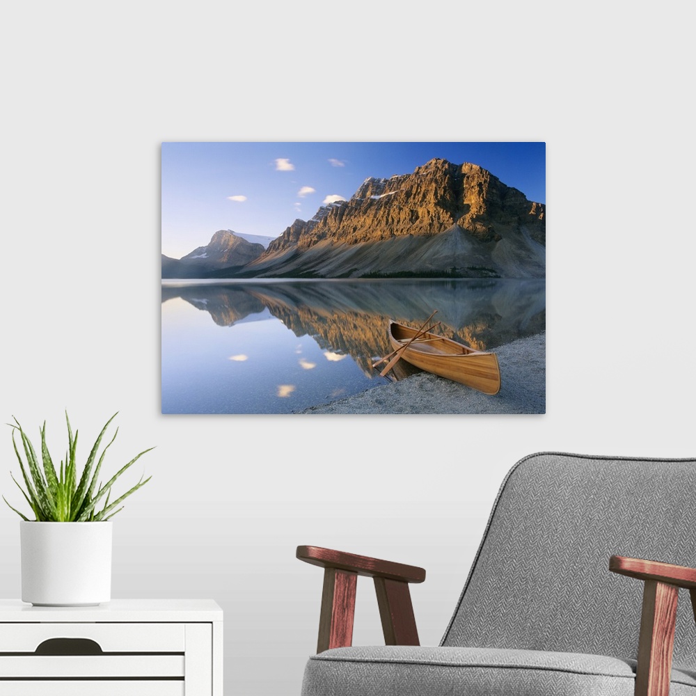 A modern room featuring Oversized photography artwork of a canoe sitting on the edge of water with mountains in the backg...