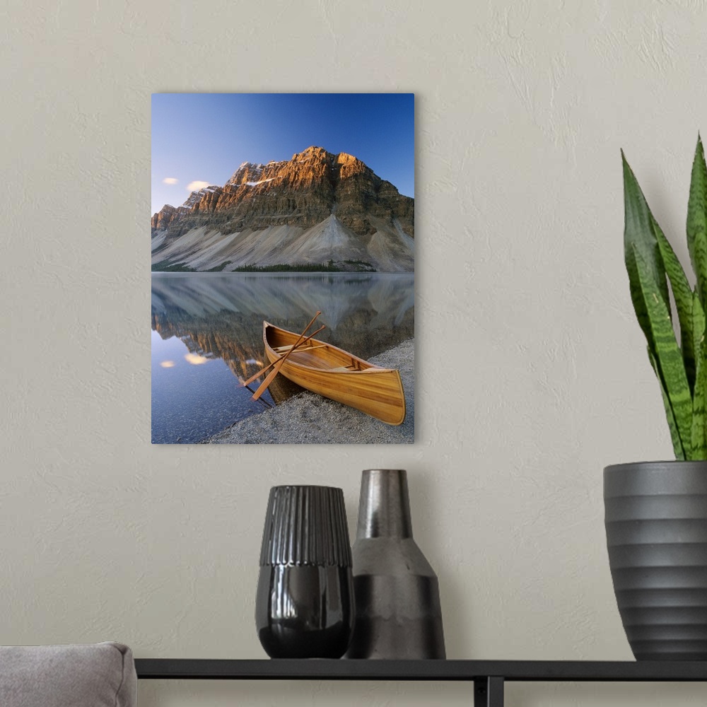A modern room featuring Vertical photograph of a boat on the shore of Bow Lake in Alberta, Canada with a mountain in the ...
