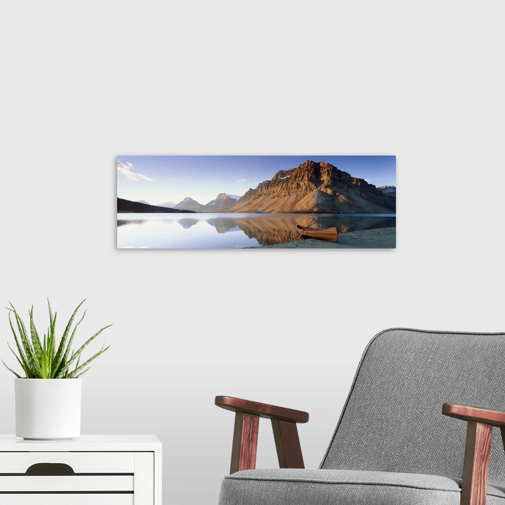 A modern room featuring Panoramic photo on canvas of a smooth lake with a wooden canoe on the shoreline and big rocky mou...