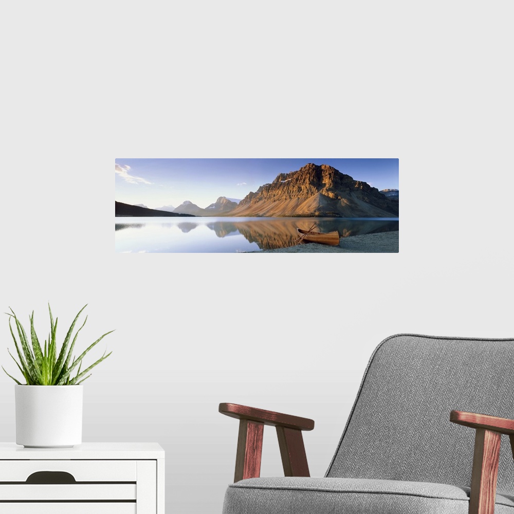 A modern room featuring Panoramic photo on canvas of a smooth lake with a wooden canoe on the shoreline and big rocky mou...