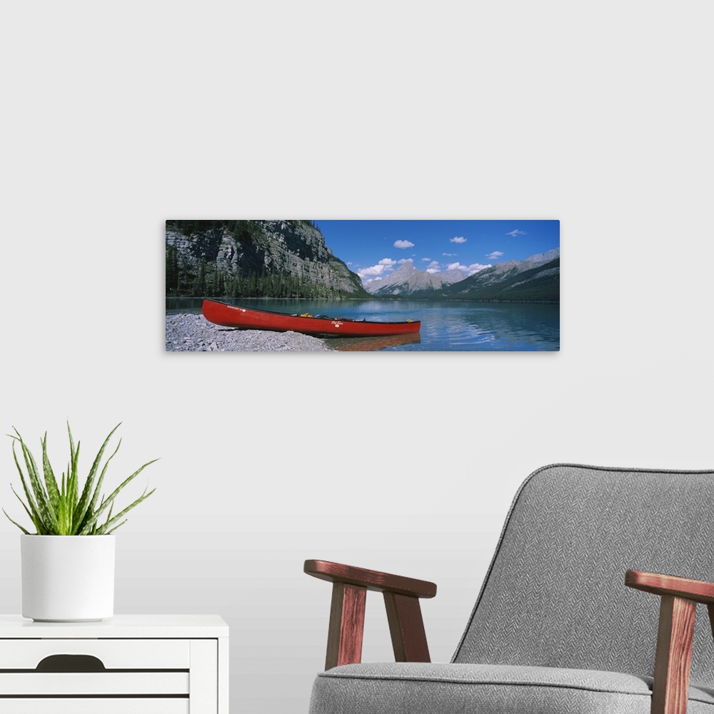 A modern room featuring A long canoe is pictured in wide angle view as it sits half in half out of the water. Mountainous...