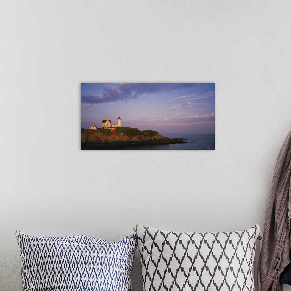 A bohemian room featuring Cape Neddick Lighthouse perched on the top of a green and rocky cliff with the warm sunset reflec...