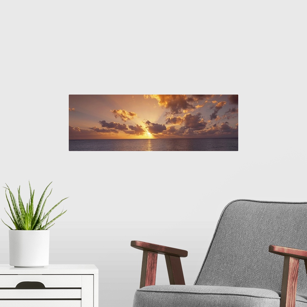 A modern room featuring Wide angle photograph of the setting suns rays beaming through a partly cloudy sky and reflecting...