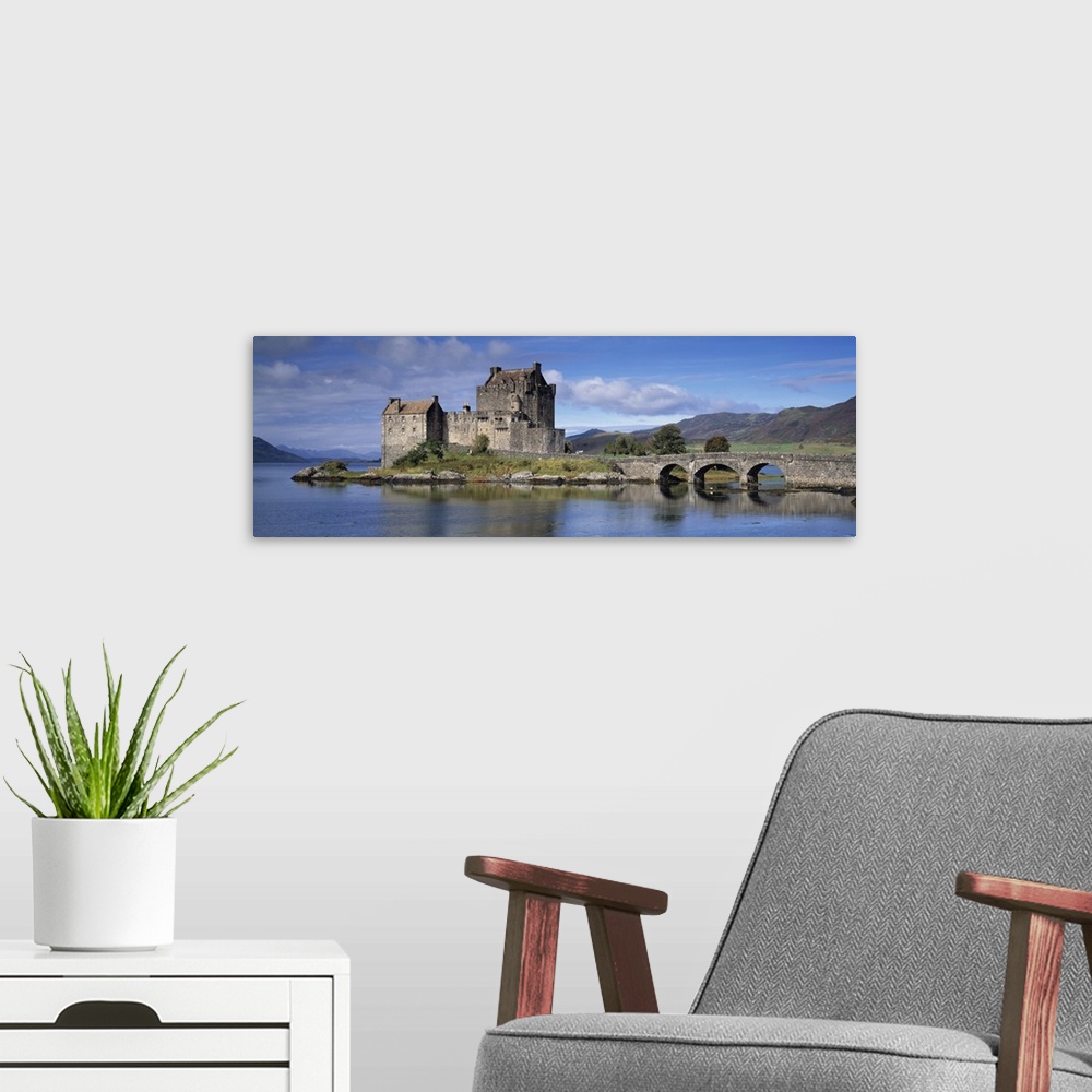 A modern room featuring Panoramic photograph of a bridge over Loch Duich, leading to a large, old castle on Eilean Donan ...