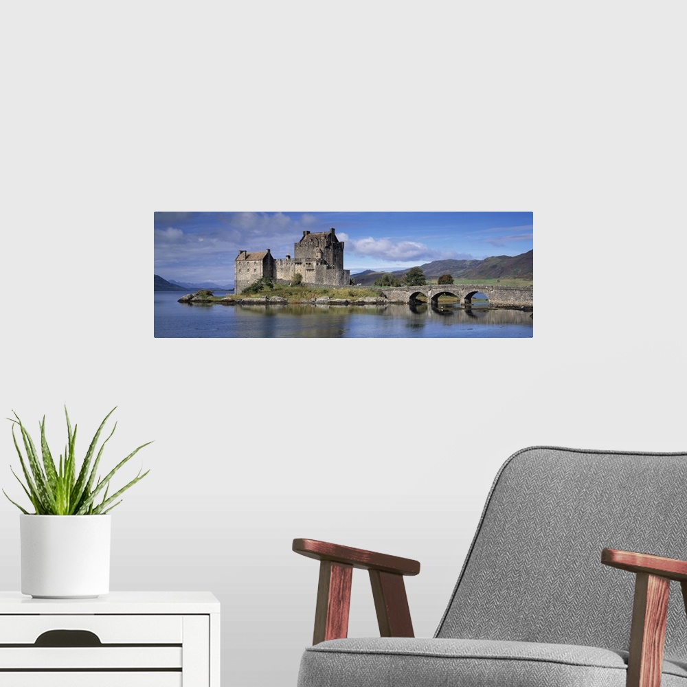 A modern room featuring Panoramic photograph of a bridge over Loch Duich, leading to a large, old castle on Eilean Donan ...