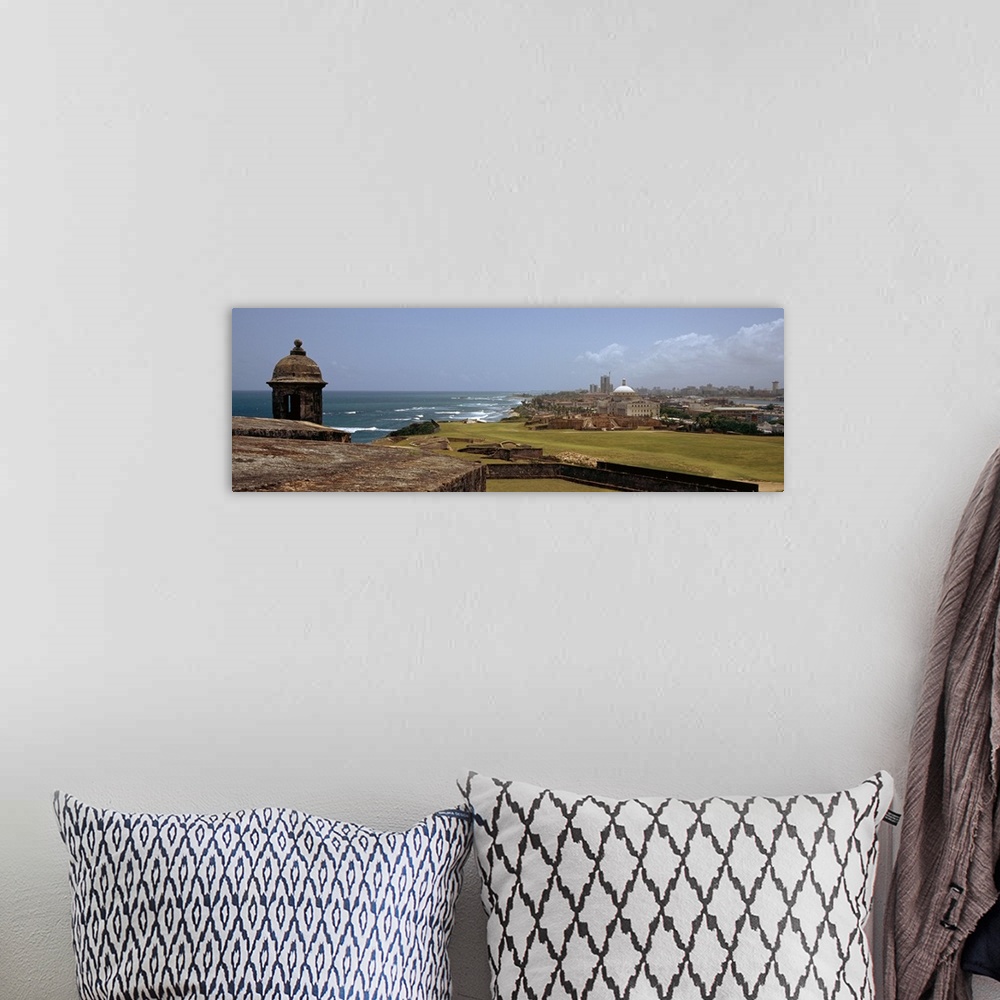A bohemian room featuring The coast of San Juan is photographed in panoramic view with the ocean to the left and the city o...