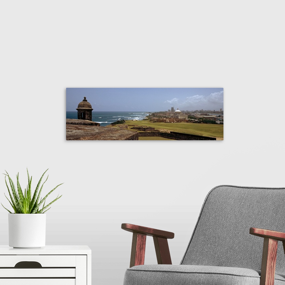 A modern room featuring The coast of San Juan is photographed in panoramic view with the ocean to the left and the city o...