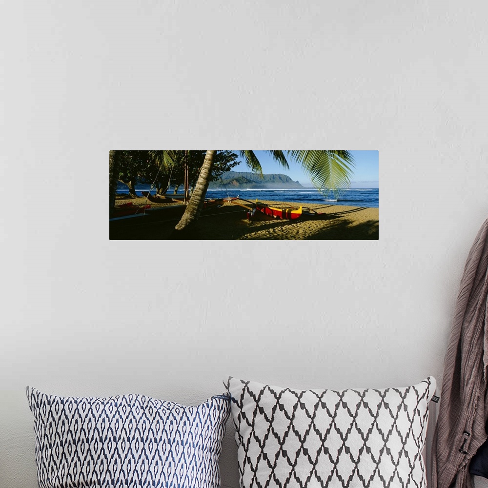 A bohemian room featuring A large panoramic photograph of a boat on the beach that is mostly covered by the shadows of palm...