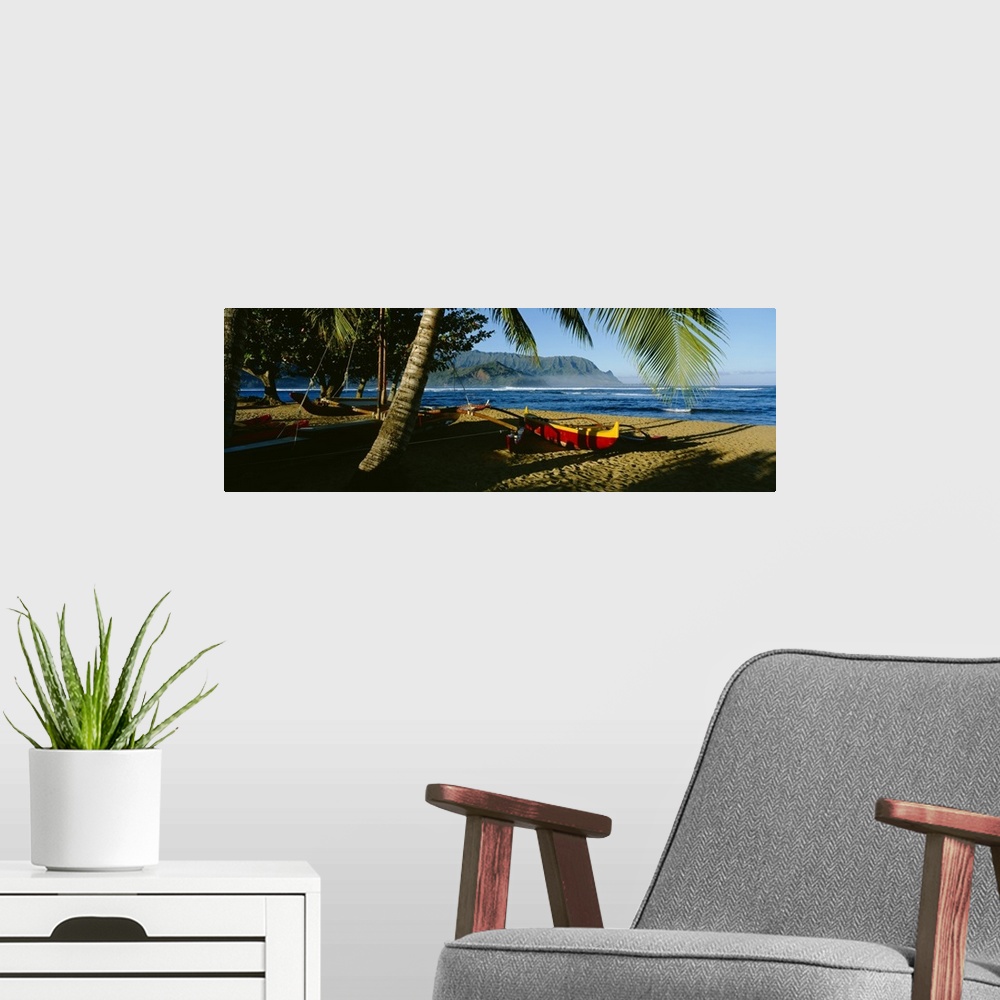 A modern room featuring A large panoramic photograph of a boat on the beach that is mostly covered by the shadows of palm...