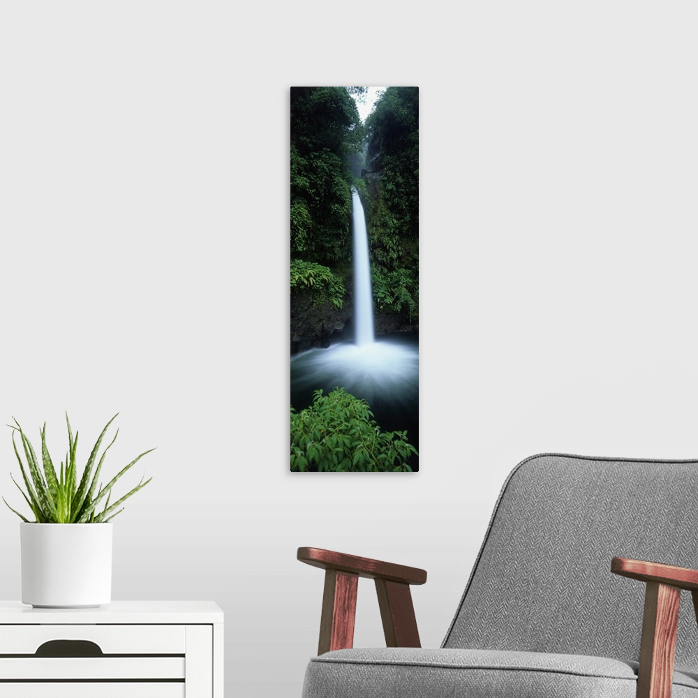 A modern room featuring Vertical canvas print of a narrow but powerful waterfall rushing down from a tropical forest.