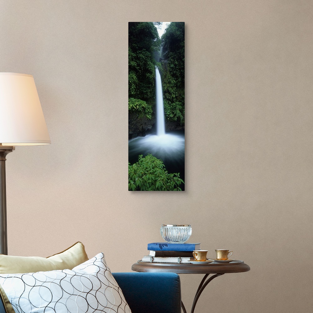 A traditional room featuring Vertical canvas print of a narrow but powerful waterfall rushing down from a tropical forest.