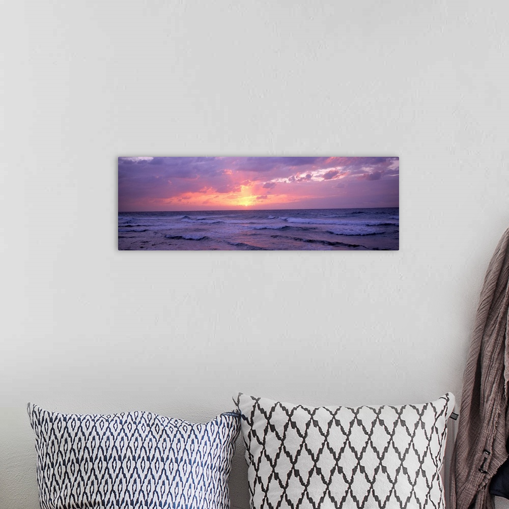 A bohemian room featuring Panoramic photograph shows the glow of the sun as it begins to set behind a group of clouds and s...