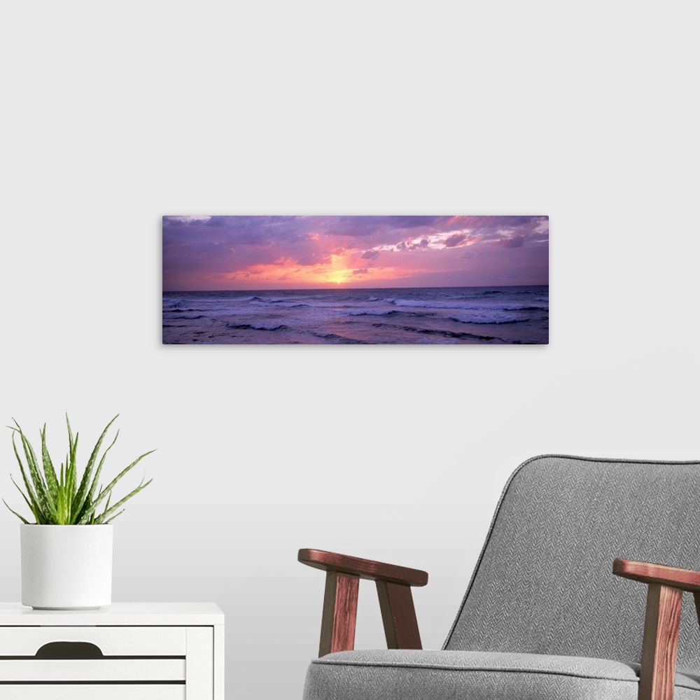 A modern room featuring Panoramic photograph shows the glow of the sun as it begins to set behind a group of clouds and s...