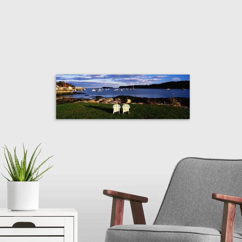 A modern room featuring Giant, landscape photograph of two wooden chairs overlooking the coastline onto many boats in blu...