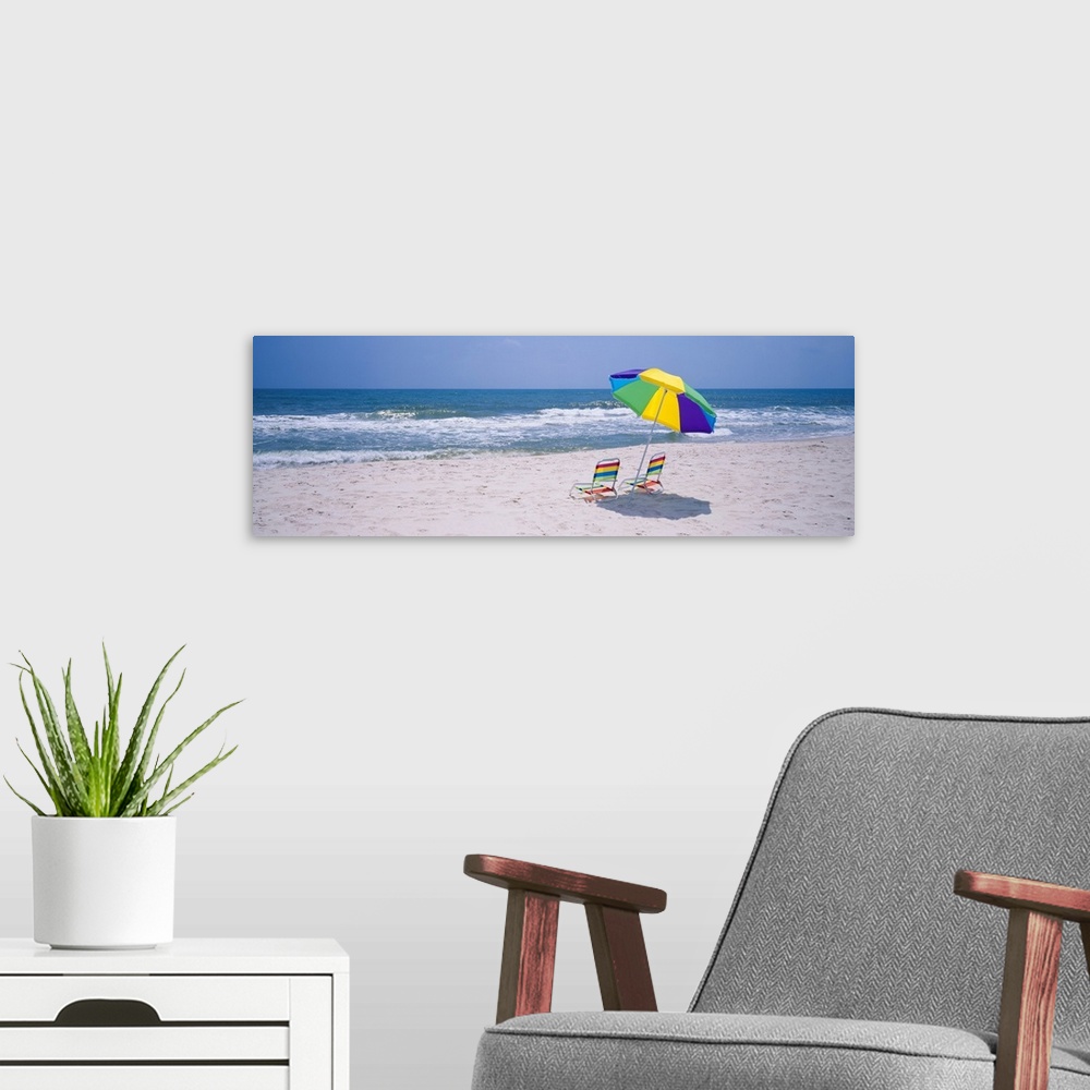 A modern room featuring Panoramic photograph includes two chairs sitting under a vibrantly colored umbrella as the waves ...