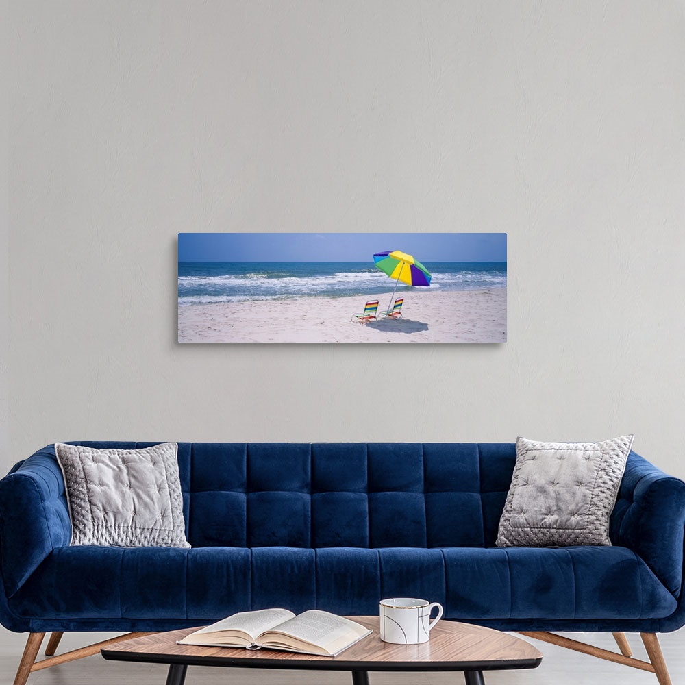 A modern room featuring Panoramic photograph includes two chairs sitting under a vibrantly colored umbrella as the waves ...