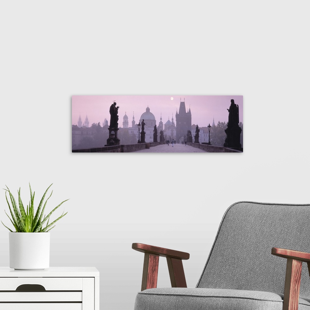 A modern room featuring Horizontal photo print of a bridge with people walking across amongst statues and an old town in ...