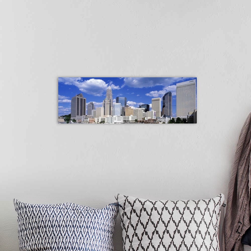 A bohemian room featuring Puffy clouds float above modern skyscrapers in a skyline of the most populous city in North Carol...