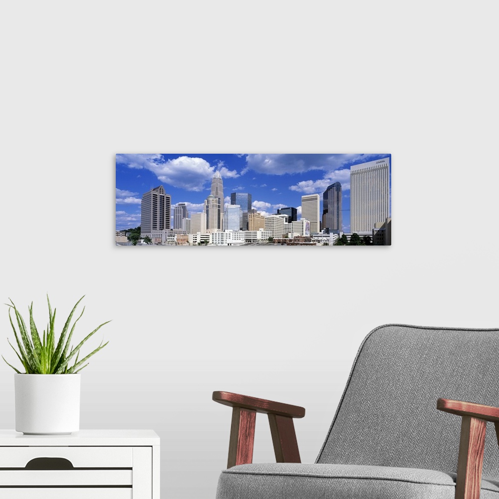A modern room featuring Puffy clouds float above modern skyscrapers in a skyline of the most populous city in North Carol...