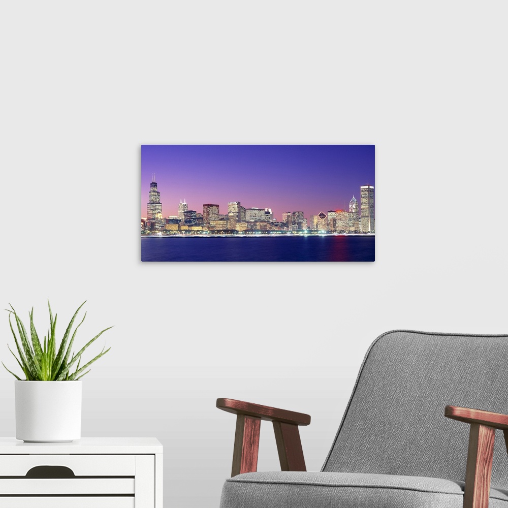 A modern room featuring Large photo on canvas of a lit up cityscape by the waterfront at dusk.