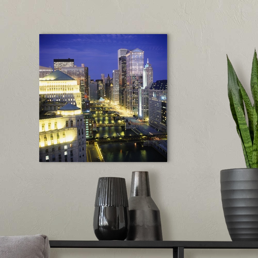 A modern room featuring Large, square photograph of the Chicago River surrounded by lit skyscrapers on three sides, at ni...