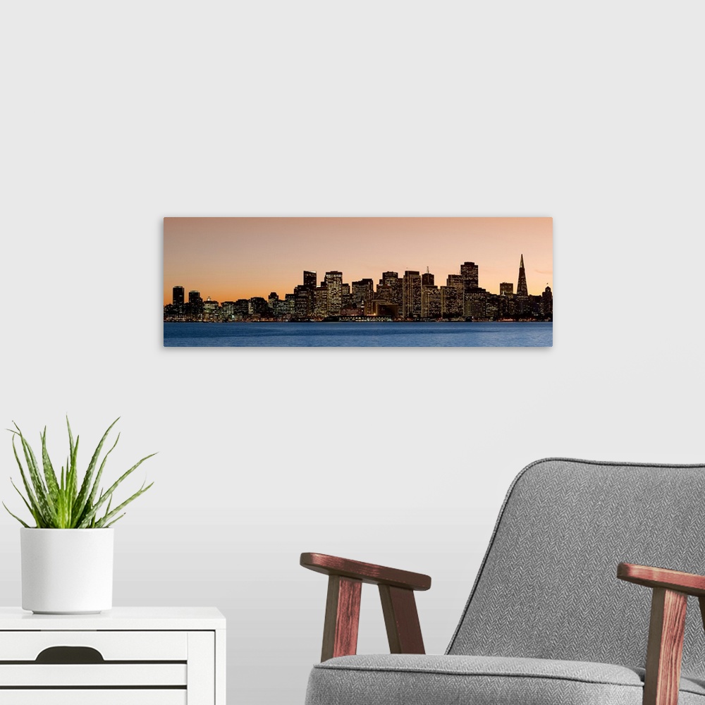 A modern room featuring Horizontal image on canvas of the San Francisco skyline lit up at sunset by the water.