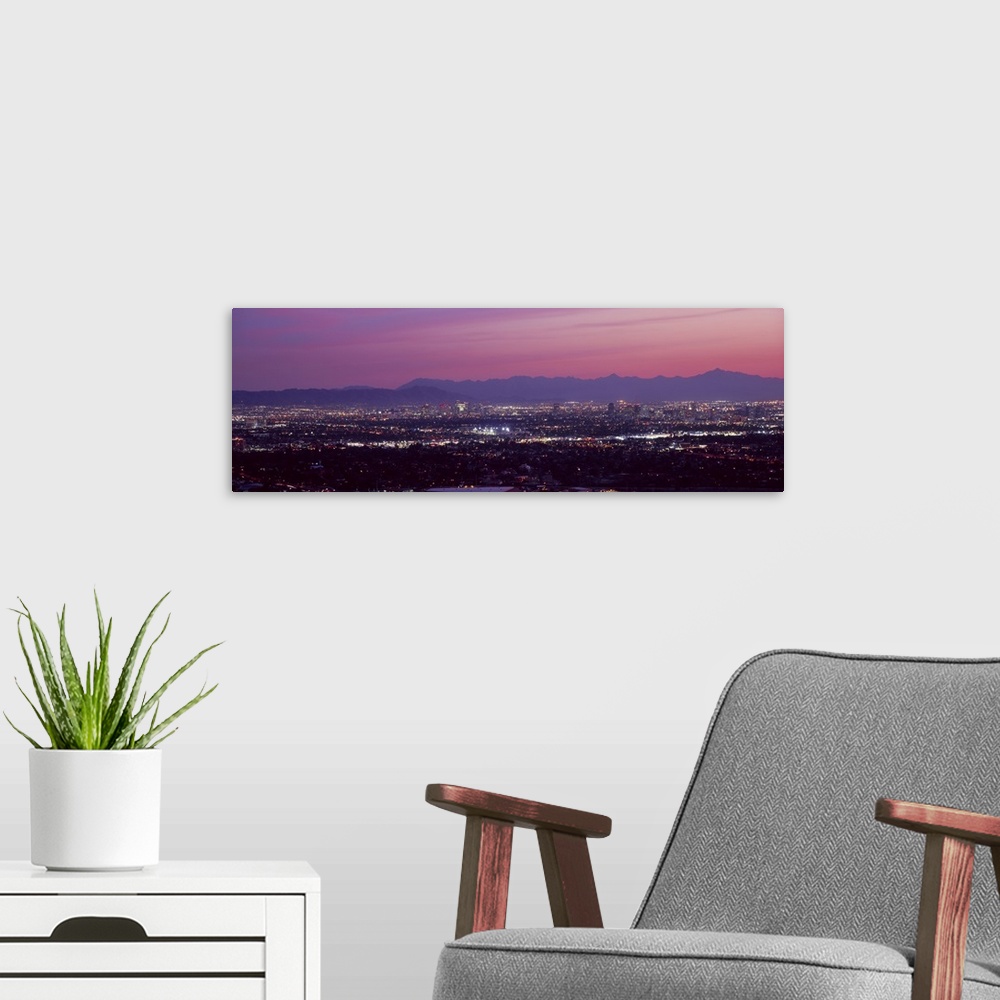 A modern room featuring The city of Phoenix is illuminated under a dusk sky and shot in a panoramic view to show majority...