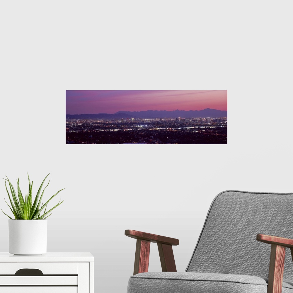 A modern room featuring The city of Phoenix is illuminated under a dusk sky and shot in a panoramic view to show majority...