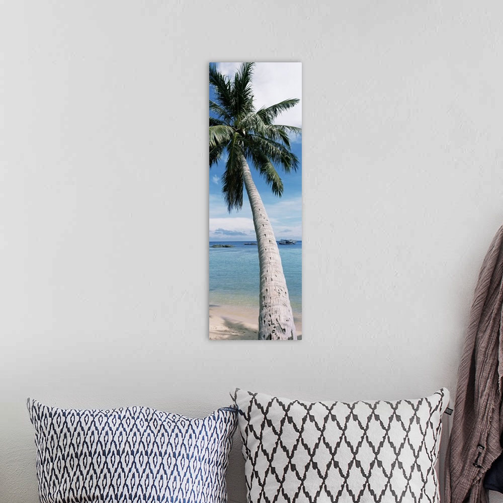 A bohemian room featuring A vertical, panoramic shaped canvas of a single tree in front of a tropical ocean and anchored boat.