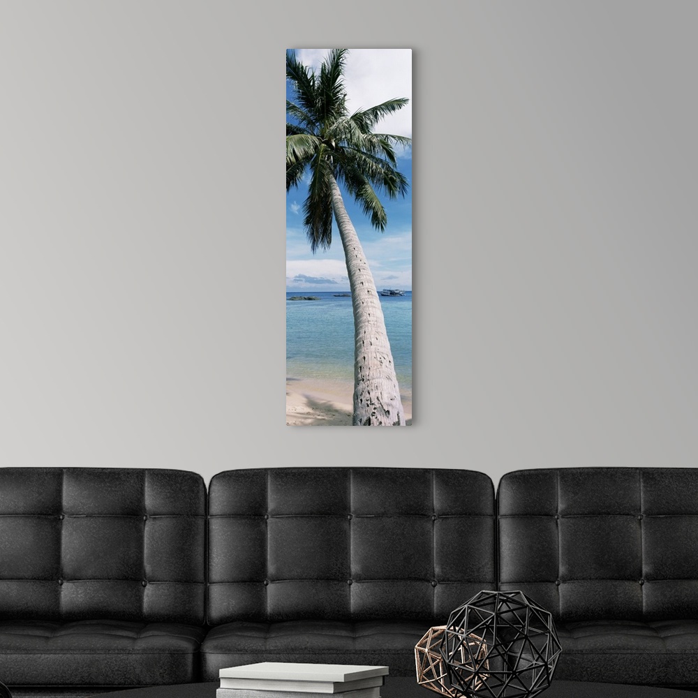 A modern room featuring A vertical, panoramic shaped canvas of a single tree in front of a tropical ocean and anchored boat.