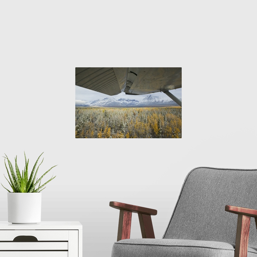 A modern room featuring A photograph is taken closely under the wing of an airplane as it glides over snow covered trees....