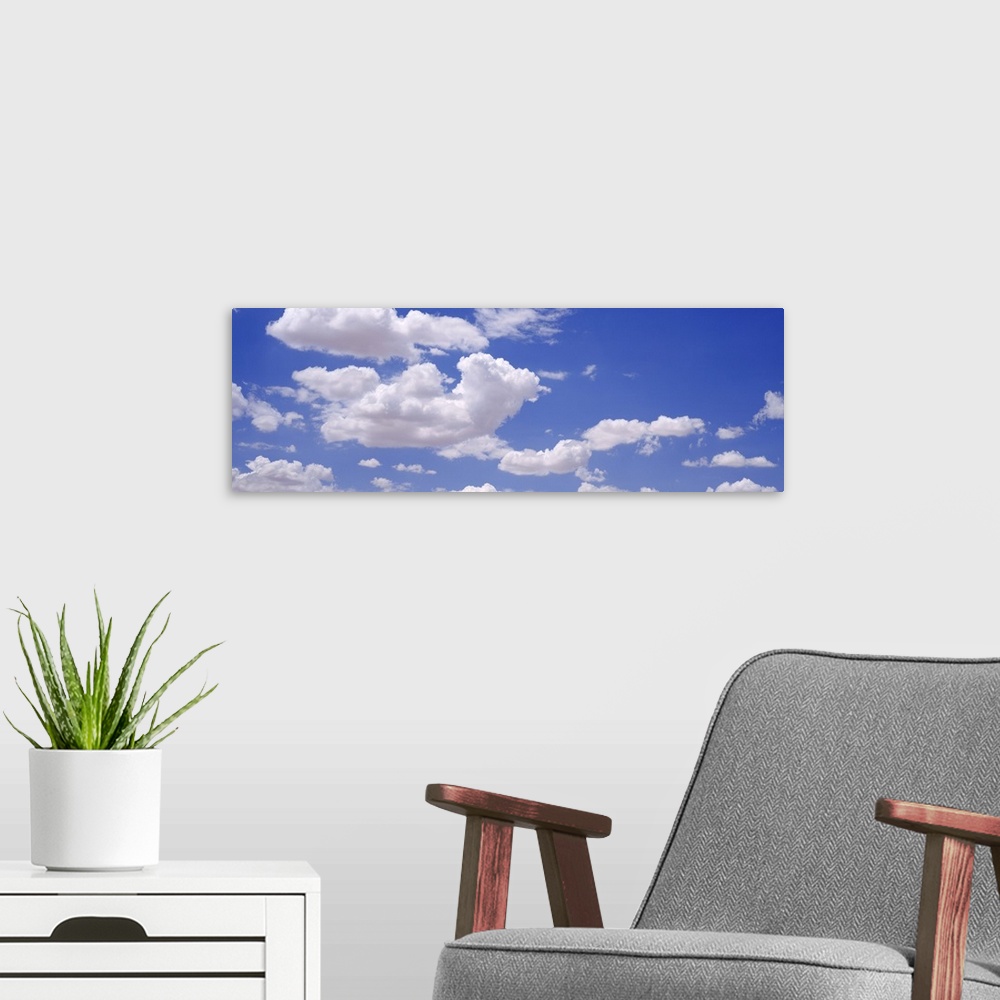 A modern room featuring Giant, landscape photograph of a light blue sky with large, fluffy, white clouds.