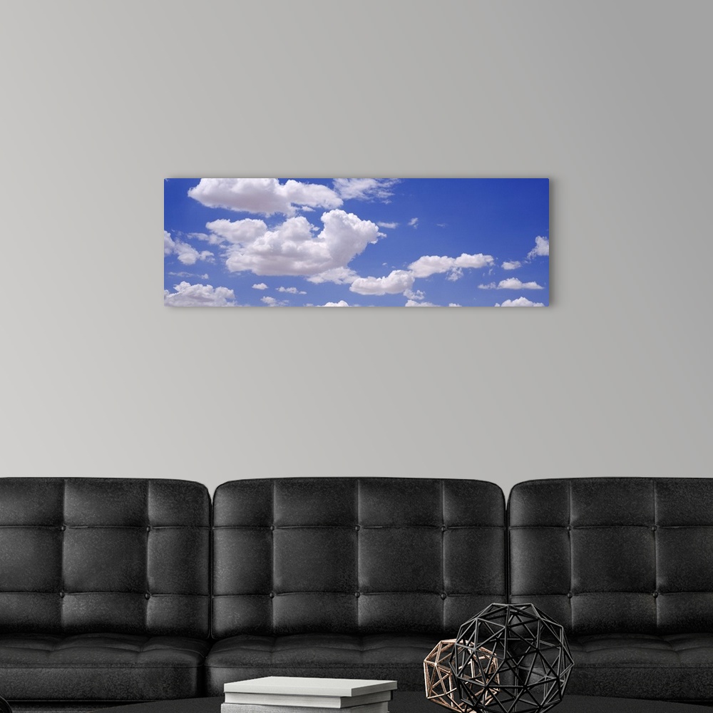 A modern room featuring Giant, landscape photograph of a light blue sky with large, fluffy, white clouds.