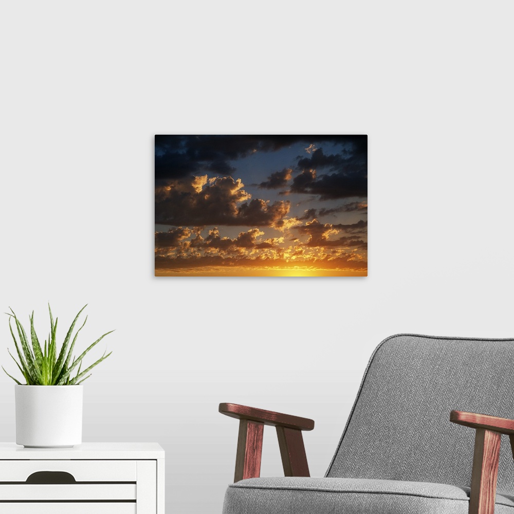 A modern room featuring Horizontal photograph on a large canvas of a vibrant, golden sunset beneath a darkening sky full ...