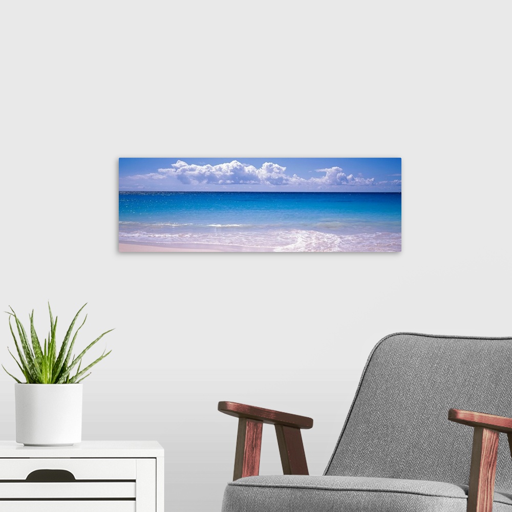 A modern room featuring Panoramic photograph shows the sparkly water of an ocean slowly coming into shore on a bright and...