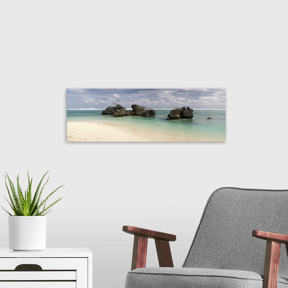 A modern room featuring Long horizontal image print of a clear ocean washing ashore past big rocks sticking out of the wa...