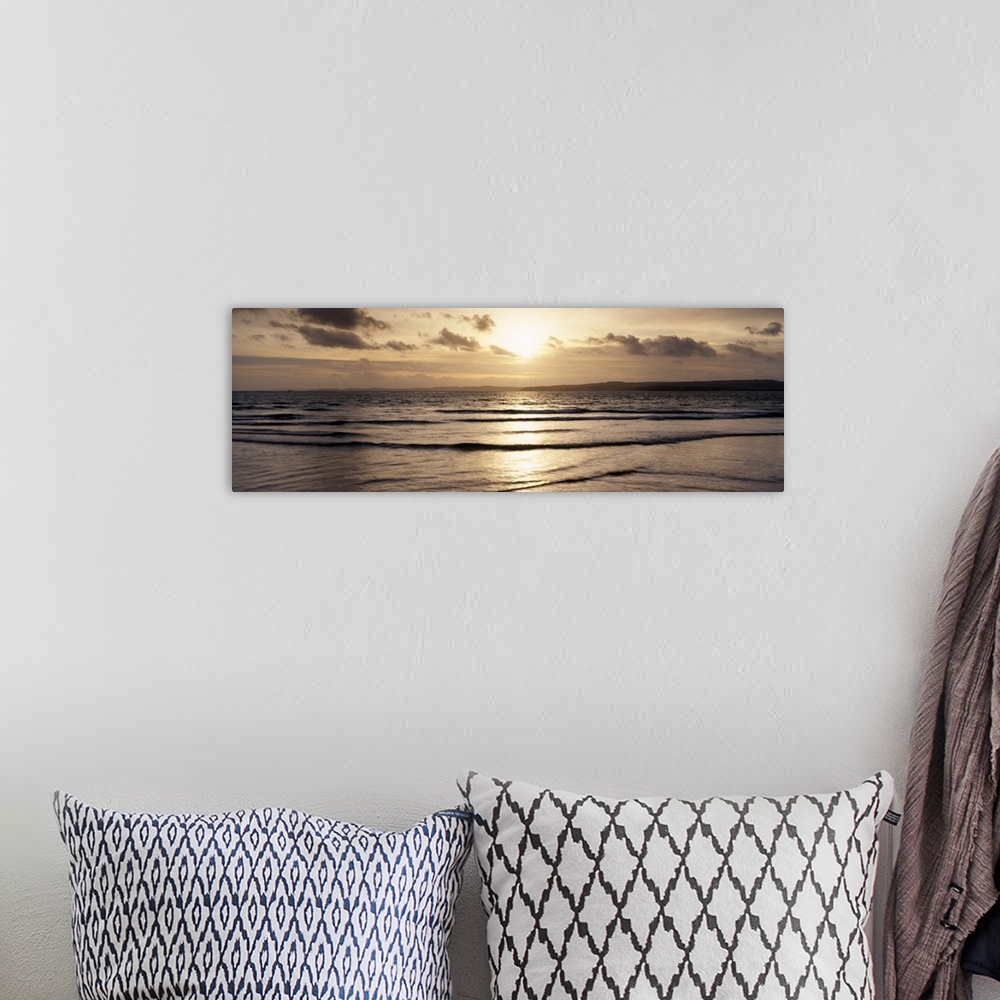 A bohemian room featuring Panoramic photo of the setting sun shining down on the ocean and beach.