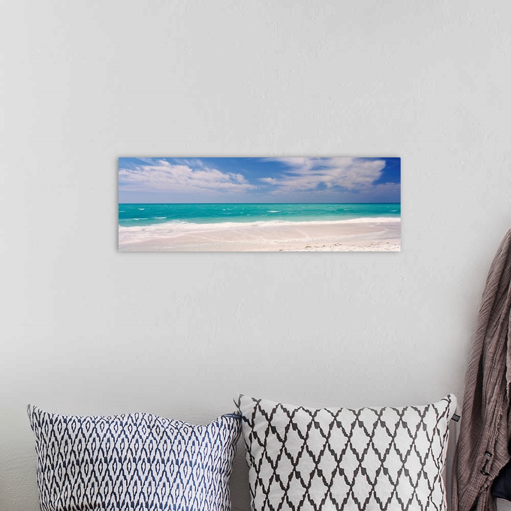A bohemian room featuring Panoramic photograph of calm ocean with surf and sand in the foreground and cloudy sky above.