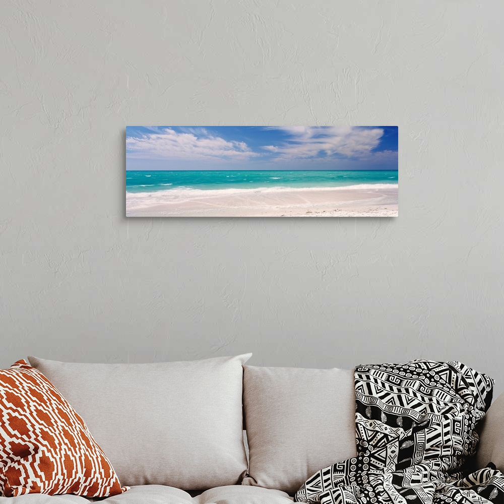 A bohemian room featuring Panoramic photograph of calm ocean with surf and sand in the foreground and cloudy sky above.