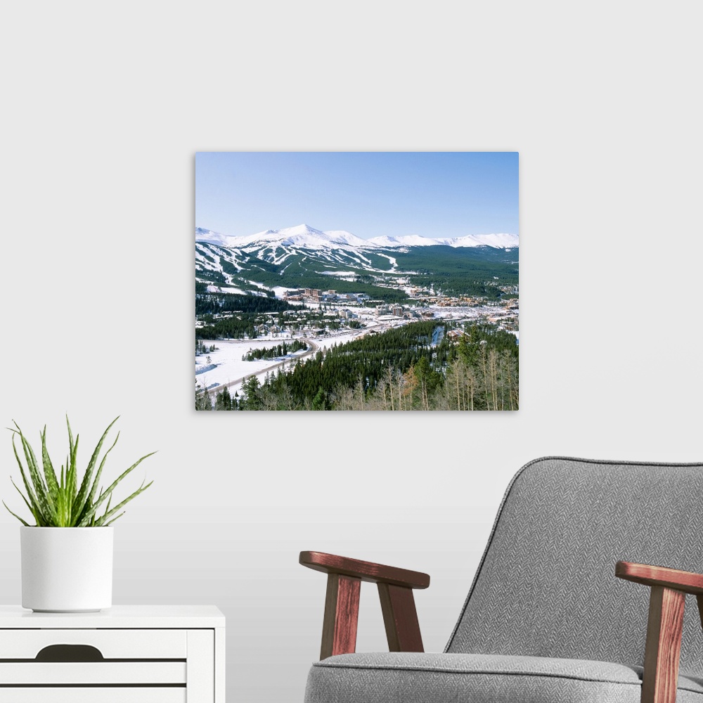 A modern room featuring Photograph of aerial view of city that is covered in snow with mountains in the distance and fore...