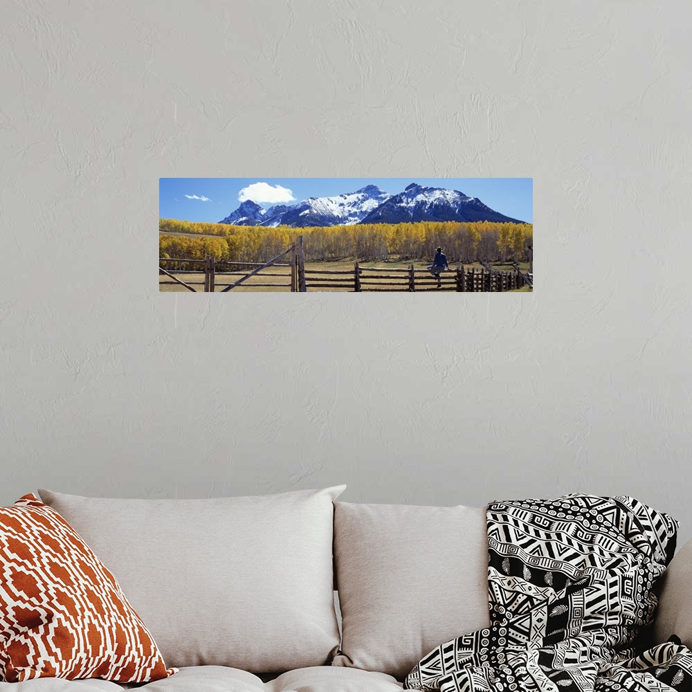 A bohemian room featuring Large panoramic image of a cowboy sitting a top a pasture fence looking towards the fall colored ...