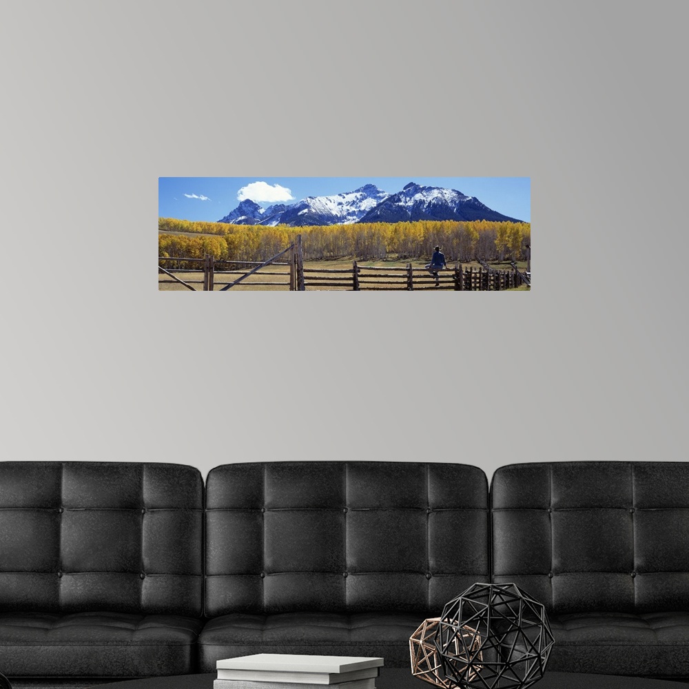 A modern room featuring Large panoramic image of a cowboy sitting a top a pasture fence looking towards the fall colored ...